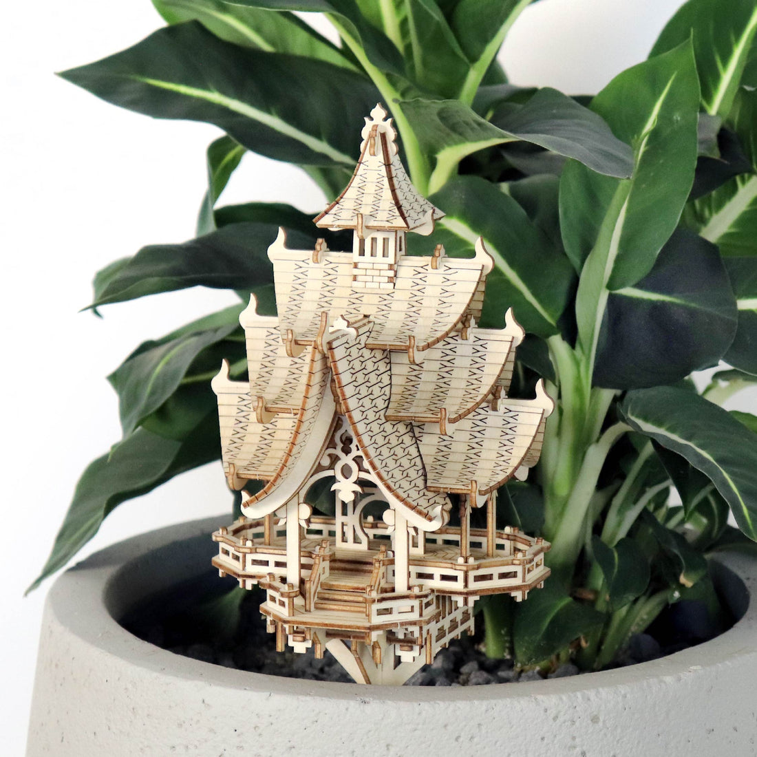 A completed Tiny Treehouse wooden model kit, resembling a flat-base treehouse, placed inside a real plant pot, showcasing intricate details and LED lights.